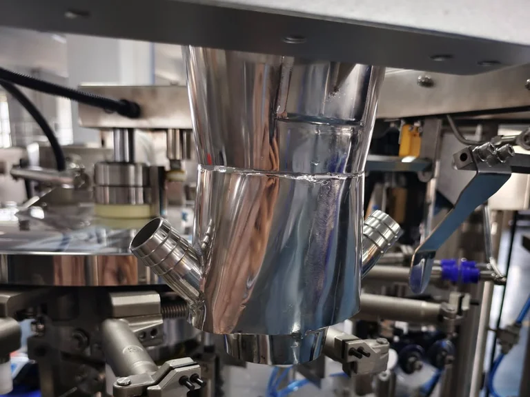 Stainless steel liquid filling funnel with hose inlets above the pouch carousel of a premade pouch machine