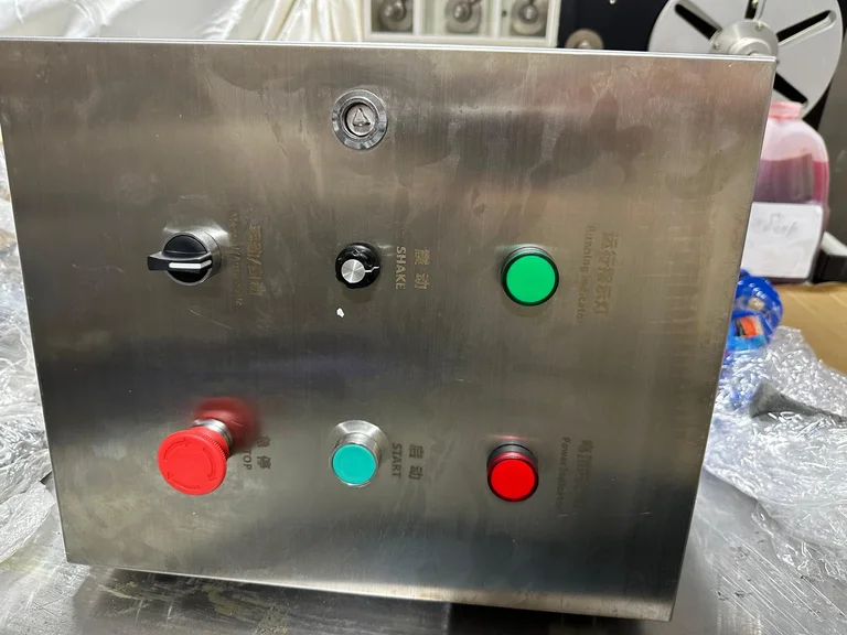 Stainless steel control box with a selector switch, a shake knob, start and stop buttons and indicator lamps, unpacked on a plastic-wrapped base
