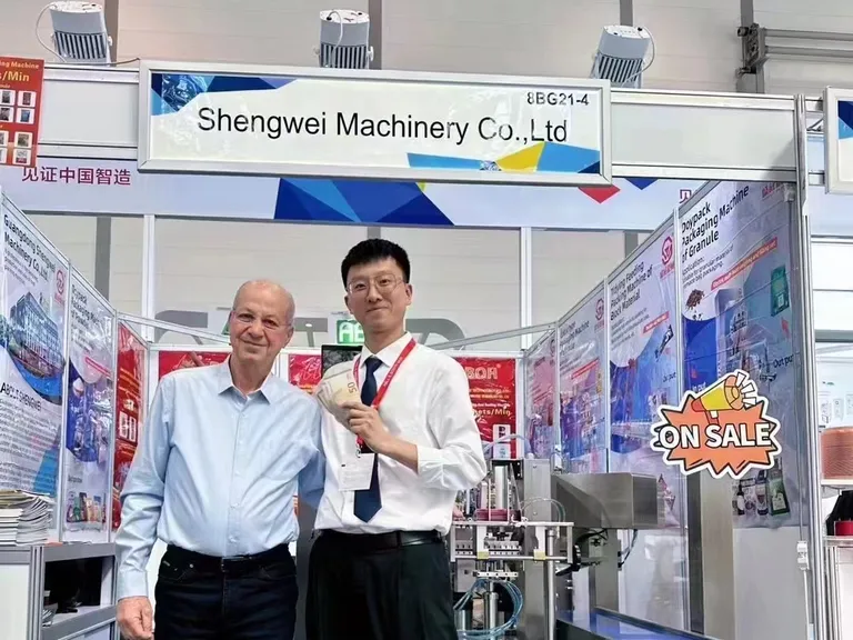Stand 8BG21-4 de ShengWei Machine en interpack 2023 — máquina de bolsas prefabricadas con un miembro del equipo y un cliente